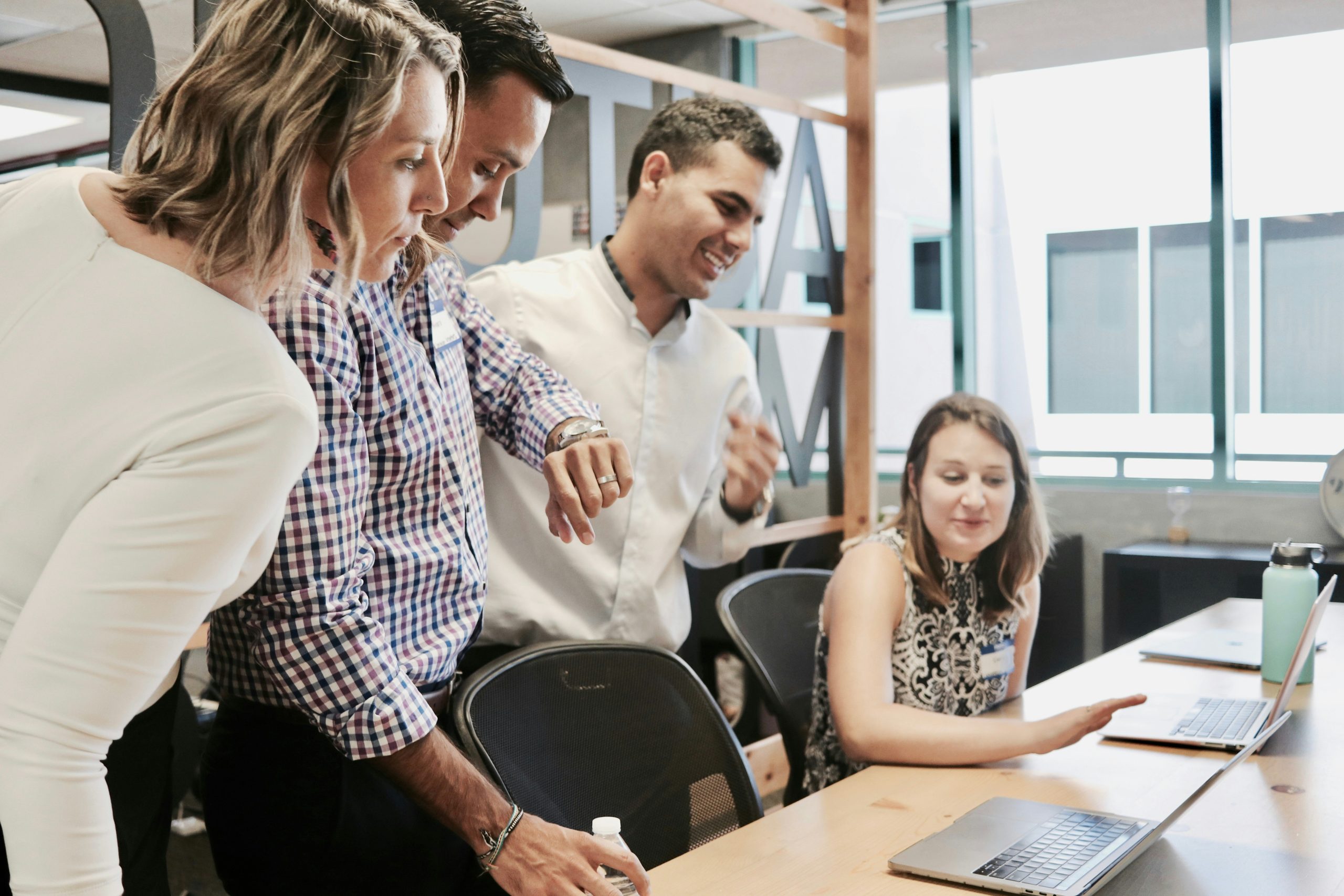 A diverse group of four professionals collaborating at a table in a modern office, smiling and reviewing documents, illustrating teamwork in creating a competency framework.